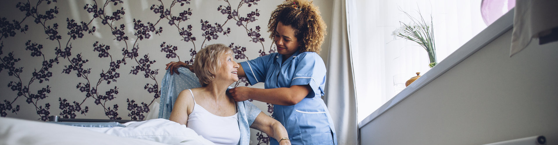 Caregiver helping a senior woman get dressed in her bedroom